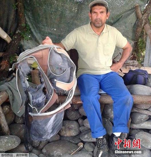 圖為當?shù)貢r間7月30日，留尼旺島上的一名海岸清潔人員展示他找到的一個手提箱的殘骸。